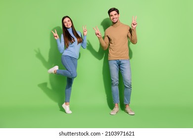 Photo of two friendly people posing make v-signs cheerful smile wear casual outfit isolated green color background