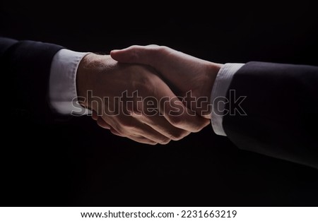 Photo of two men in suits shaking hands on a black background