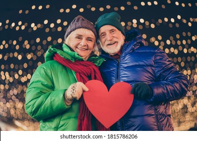 Photo Of Two Parents People Old Woman Man Have X-mas Christmas Spirit Party Date Hold Big Paper Card Heart Gift Under Evening Lights Outdoors Wear Scarf Outerwear Headwear