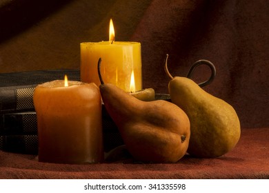 Photo of two pears placed in front of two candles and some books shot in studio on a light brown background