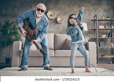 Photo of two people funky grandpa play guitar small nice granddaughter mic singing cool style sun specs denim clothes repetition school concert stay home quarantine living room indoors