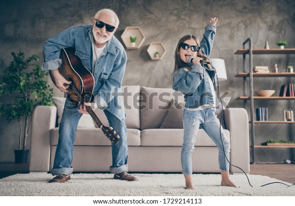 Photo of\
two people funky grandpa play guitar small nice granddaughter mic\
singing cool style sun specs denim clothes repetition school\
concert stay home quarantine living room\
indoors