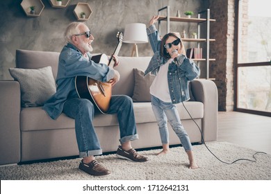 Photo of two people grandpa play guitar little granddaughter mic singing rejoicing cool style trendy sun specs denim clothes repetition school concert stay home quarantine living room indoors