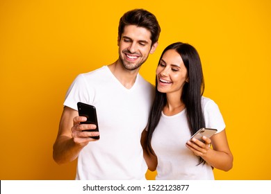 Photo of two people holding telephones watching funny humorous video wear casual clothes isolated yellow color background
