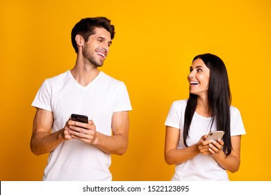 Photo of two people holding telephones checking feednews laughing about good joke wear casual clothes isolated yellow color background