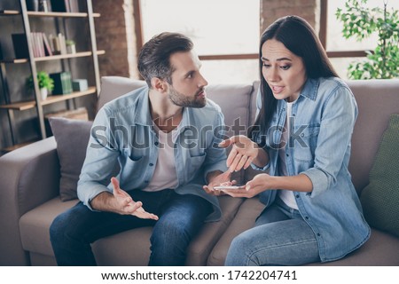 Photo of two people woman use smartphone try explain envy angry husband she dont have another man point hand screen feel confused sit comfort cozy couch in house indoors