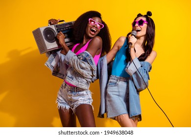 Photo of two positive cute ladies hold retro boombox mic sing wear sunglass jeans outfit isolated yellow color background