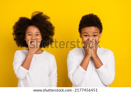 Photo of two positive excited siblings hand cover mouth laugh tease isolated on yellow color background