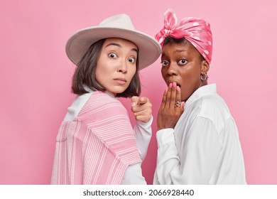 Photo of two shocked young women stand sideways look with widen eyes from curiosity notice shocking announcement wear fashionable clothes isolated over pink background have anxious expressions