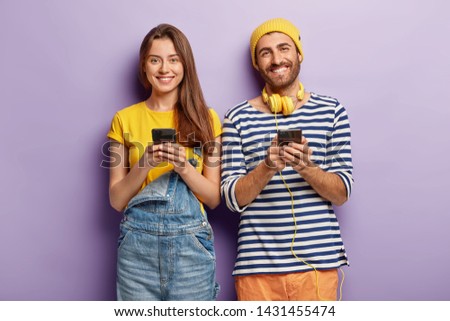 Photo of two smartphone geeks use modern technologies for posting new photos in social networks, connected to wireless internet check notification. Woman in overalls spends leisure time with boyfriend