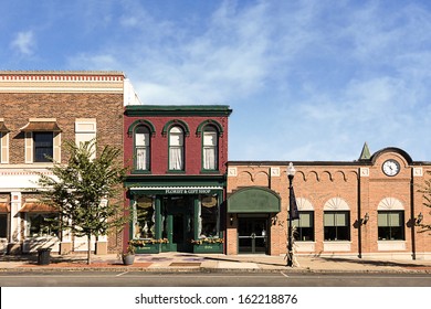 A photo of a typical small town main street in the United States of America. Features old brick buildings with specialty shops and restaurants. Decorated with autumn decor. 