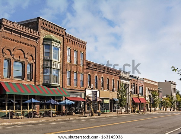A photo of a
typical small town main street in the United States of America.
Features old brick buildings with specialty shops and restaurants.
Decorated with autumn decor. 