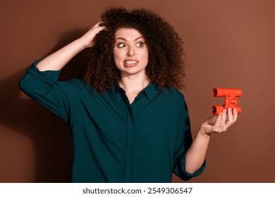 Photo of uncertain pretty lady dressed green shirt holding binoculars empty space isolated brown color background - Powered by Shutterstock