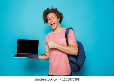 Photo Of University Guy With Curly Hair Wearing Casual Clothing And Backpack Holding Open Laptop And Showing Thumb Up Isolated Over Blue Background