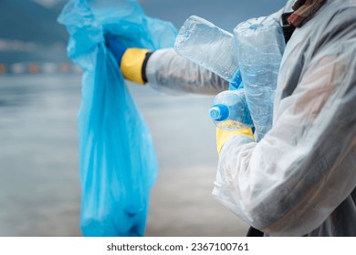 Photo of unknown person while holding garbage bag and plastic bottles in arms.