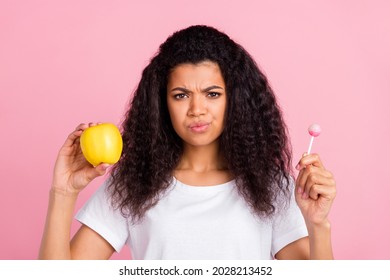 Photo Of Unsure Pretty Dark Skin Lady Wear White T-shirt Choosing Eating Caramel Apple Isolated Pink Color Background