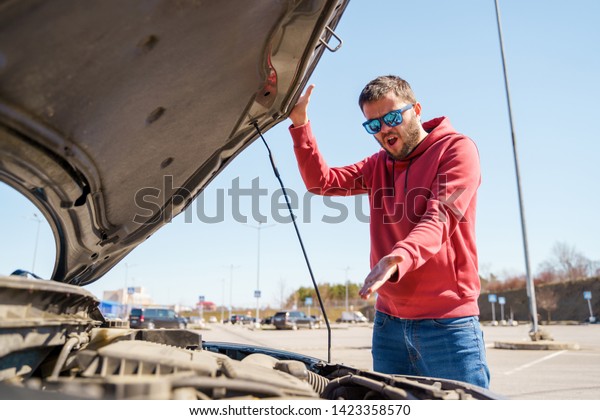 Photo of upset man next to open hood of broken\
car in daytime