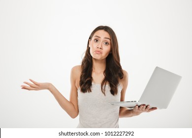 Photo Of Upset Woman With Long Brown Hair Throwing Up Hands And Expressing Confusion While Holding Silver Personal Computer Isolated Over White Wall