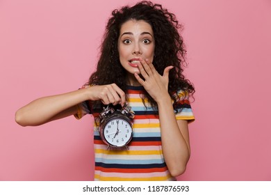 Photo Of Uptight Woman 20s With Curly Hair Holding Alarm Clock Isolated Over Pink Background