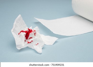 A photo of used bloody toilet paper and a toilet paper roll on the light blue background. Blood drops and traces. Hemorrhoids, constipation treatment health problems. Menstrual or hemorrhoids bleeding
