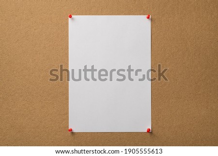 Photo of vertical clear sheep of paper attached with red pins to the wooden board