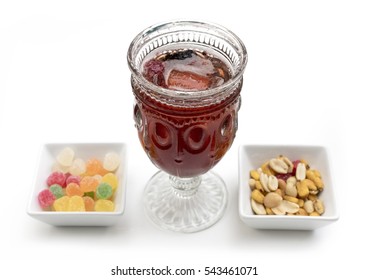 A photo of a vibrant red cocktail with gum drops and salted peanuts for snacks, on white background. Selective focus