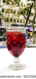 A photo of a vibrant red cocktail with a straw on a cafe terrace table, with blurred city lights in the background