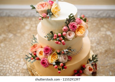 Photo of wedding cake with gold plating. The three-tiered cake for the wedding is painted with beautiful large live flowers.