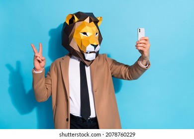 Photo of weird bizarre guy in lion mask taking selfie smart phone make v-sign halloween event isolated over blue color background