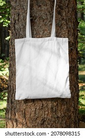 Photo Of White Blank Tote Bag Hanging On Tree In Forest. Outdoor Minimal Clothing Product Apparel Style Business. Photo Template For Mockup, Print Store, E-commerce Shop, Branding Design Project.