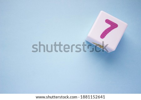 Photo of a white plastic cube with a purple number 7 on a blue background in the upper right corner. With copy space