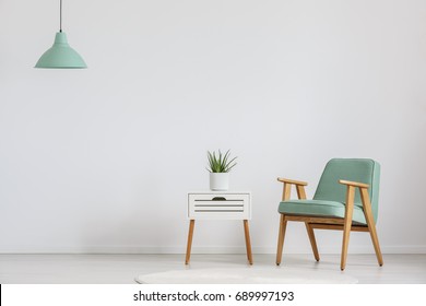 Foto von weißem Holzschrank mit frischer Pflanze und minzem Lampenschirm