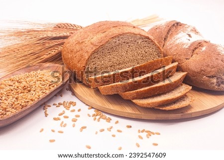 Photo of whole wheat breads, wheat ears and wheat grains and wooden container full of wheat on white background.