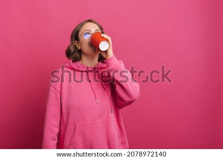 A photo of a woman enjoying her cup of coffee near a pink wall .