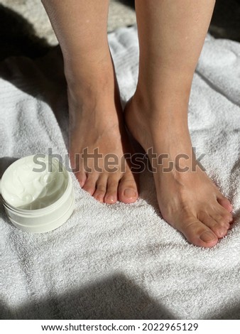 Photo of woman feet on white towel with lotion beside