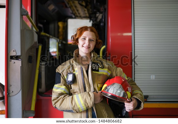 Photo of woman firefighter with helmet in hands\
against backdrop of fire\
truck