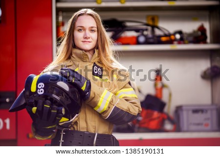 Photo of woman firefighter with helmet in her hands standing near fire truck