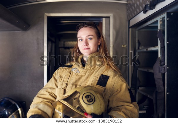 Photo of woman firefighter with helmet in her hands\
standing in fire truck