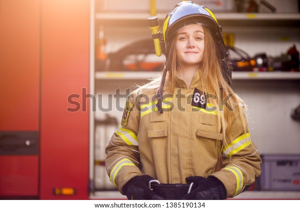 Photo of woman firefighter in helmet standing\
near fire truck at fire\
station