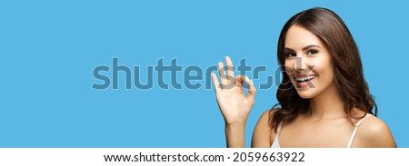 Photo of woman making ok okay hand sign or zero gesture, isolated on bright blue color background. Happy smiling gesturing brunette girl at studio. Wide horizontal banner composition. Female person.
