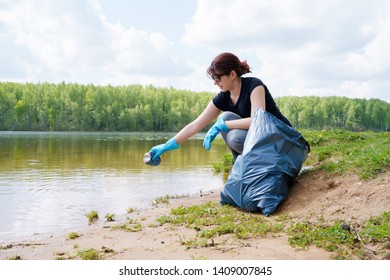 Photo of woman in rubber gloves picking up trash on river bank - Powered by Shutterstock