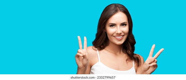 Photo of woman showing two fingers or victory hand sign gesture isolated on aqua blue green studio background. Cheerful smiling gesturing brunette girl. Wide banner composition with mock up copy space