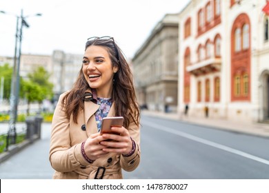 Photo of a woman using smart phone. Beautiful woman texting on the street. Beautiful woman spending time in the city. Fashionable woman with smart phone