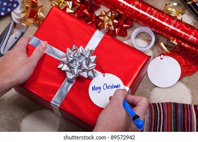 Photo of a woman writing Merry Christmas on a gift tag on a red present with silver ribbon and bow. Of course you could easily add your your message. - Powered by Shutterstock