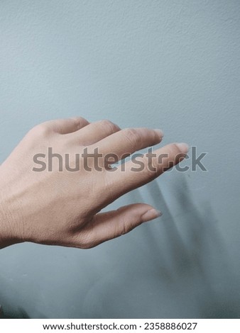 A photo of a woman's small left hand with 5 fingers slightly bent, looking weak, tan skin, not horny. Not too dark, under the gray background there is a faint shadow giving a feeling of loneliness, lo