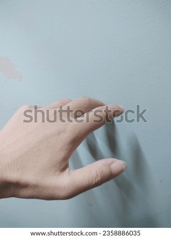 A photo of a woman's small left hand with 5 fingers slightly bent, looking weak, tan skin, not horny. Not too dark, under the gray background there is a faint shadow giving a feeling of loneliness, lo