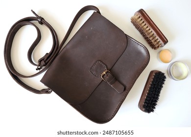 Photo of women's leather handbag Crazy Horse. Dark brown color. Next to the handbag are two brushes for cleaning the leather. Wax and cleaning products. White background. Bag has retro style scuffs.