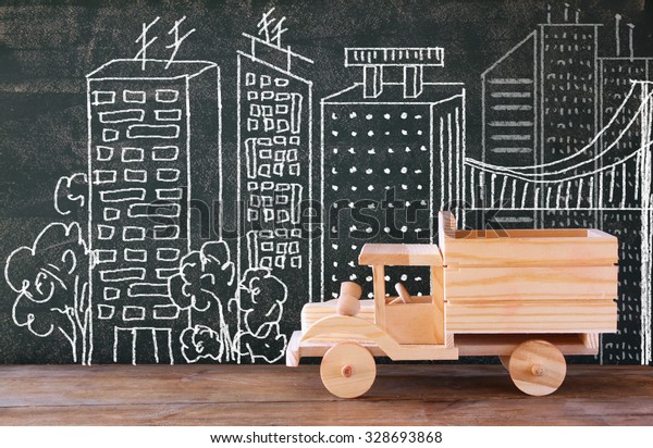photo of wooden toy truck in front of chalkboard with\
city illustration. 