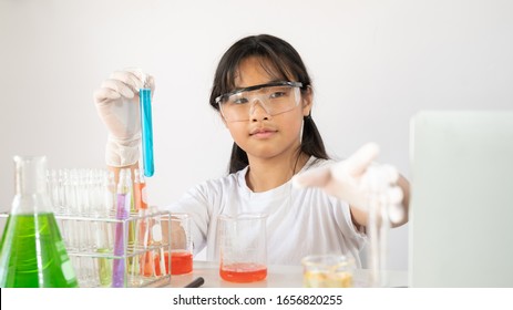 Photo of young adorable girl in safety glasses and gloves holding a flasks for chemistry while doing a scientist experiment at the modern laboratory with isolated white background.