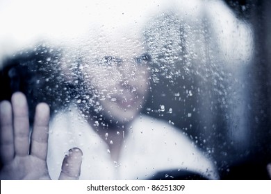photo of young adult man standing at the window on a rainy day. focus on the raindrops on the glass. toned image - Powered by Shutterstock